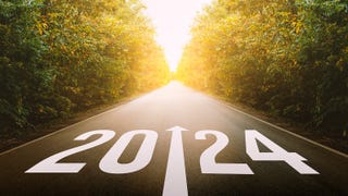 A stock photo/illustration showing a straight road narrowing into a sunny distance, flanked on either side by dense forest. On the ground at the beginning of the road, nearest the viewer, are the numbers 2024, and an arrow in the middle pointing ahead.